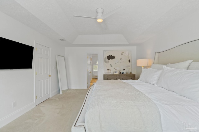 bedroom featuring light carpet, ensuite bath, a raised ceiling, a textured ceiling, and ceiling fan