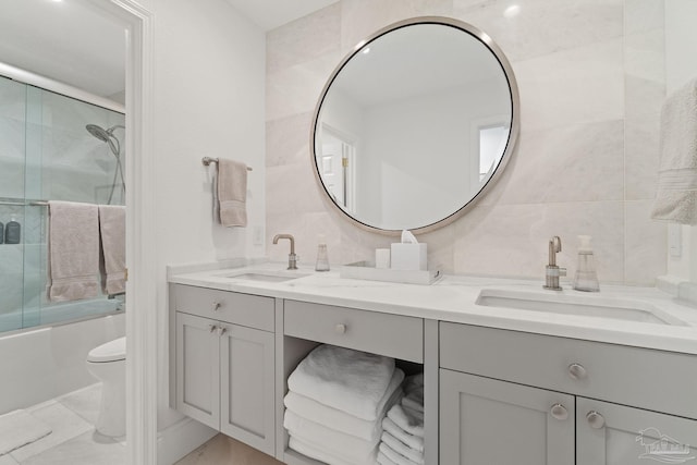 full bathroom featuring toilet, backsplash, vanity, tile walls, and combined bath / shower with glass door