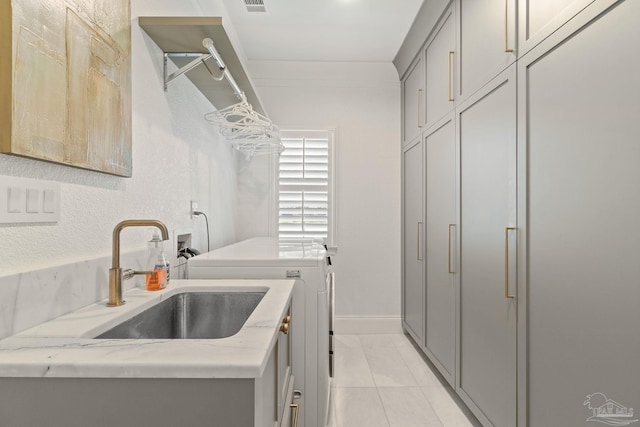 clothes washing area with sink, washer and dryer, light tile patterned flooring, and cabinets