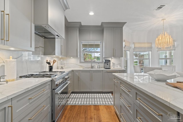 kitchen featuring a healthy amount of sunlight, wall chimney exhaust hood, light hardwood / wood-style flooring, and stainless steel range