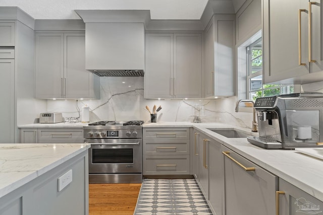 kitchen featuring gray cabinetry, light stone countertops, appliances with stainless steel finishes, sink, and premium range hood