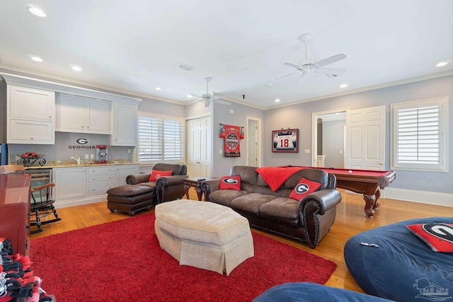 living room with light wood-type flooring, ornamental molding, pool table, ceiling fan, and indoor bar