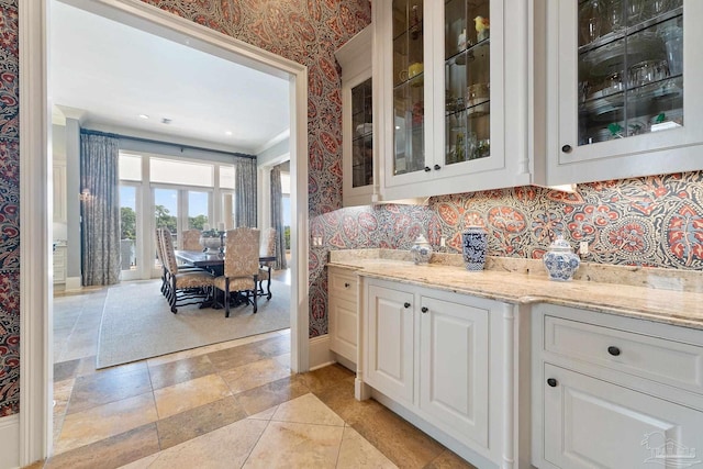 3410 N 18th Ave, Pensacola, FL 32503 - kitchen with glass insert cabinets, light stone countertops, white cabinetry, wallpapered walls, and baseboards