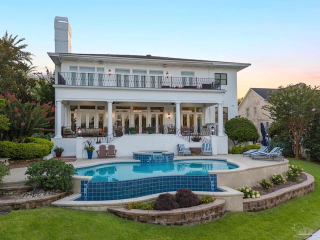 back house at dusk featuring a yard, a patio, a balcony, and a pool with hot tub