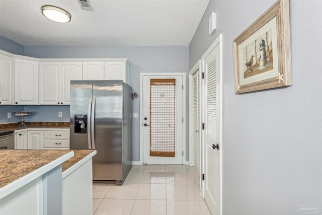 kitchen featuring stainless steel fridge, light tile patterned floors, and white cabinets