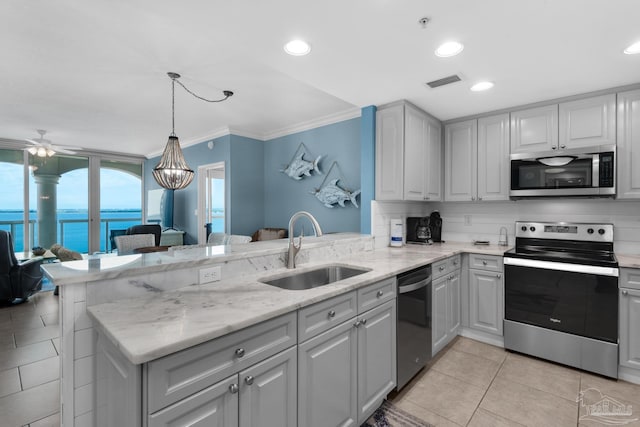 kitchen with kitchen peninsula, appliances with stainless steel finishes, ceiling fan with notable chandelier, sink, and a water view