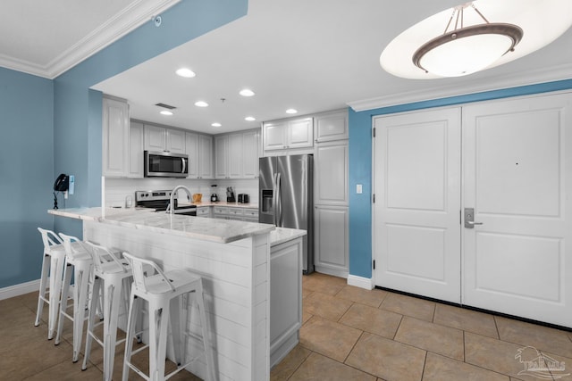 kitchen with kitchen peninsula, a kitchen bar, stainless steel appliances, crown molding, and light tile patterned floors