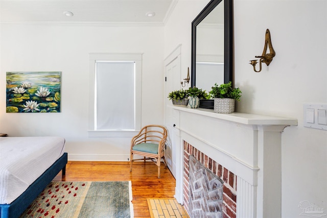 bedroom featuring a brick fireplace, crown molding, and light wood-type flooring