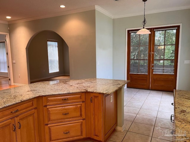 kitchen with light tile patterned floors, crown molding, light stone counters, and decorative light fixtures