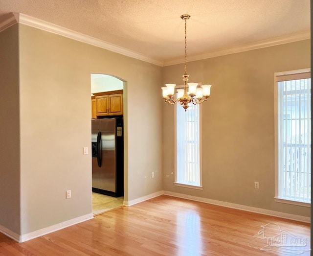 empty room featuring light wood-type flooring, ornamental molding, an inviting chandelier, and a textured ceiling