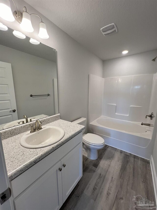 full bathroom featuring wood-type flooring, vanity, toilet, bathing tub / shower combination, and a textured ceiling