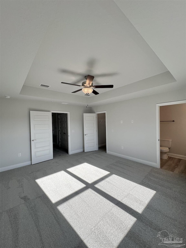 unfurnished bedroom featuring a tray ceiling, a walk in closet, ceiling fan, and carpet flooring