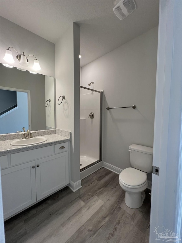 bathroom featuring wood-type flooring, toilet, a shower with door, and vanity