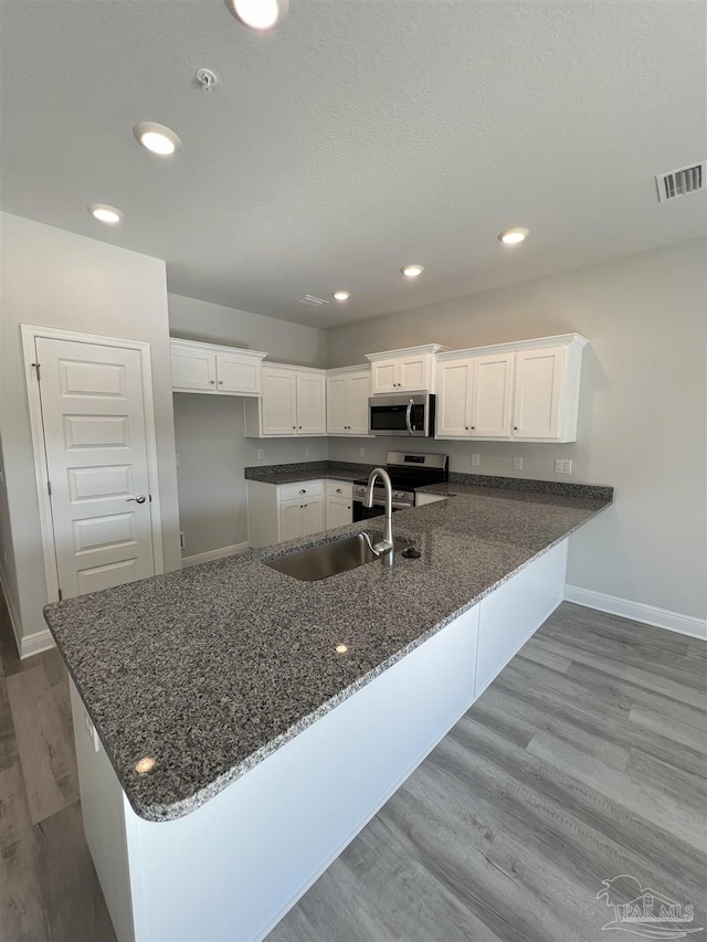 kitchen with appliances with stainless steel finishes, sink, white cabinets, and kitchen peninsula