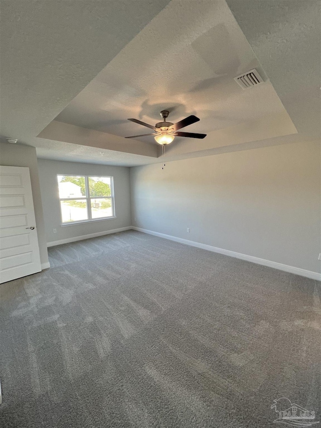 unfurnished room with a raised ceiling, ceiling fan, carpet flooring, and a textured ceiling