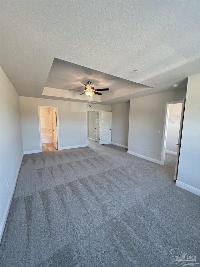 unfurnished bedroom featuring ceiling fan, ensuite bathroom, carpet, a textured ceiling, and a raised ceiling