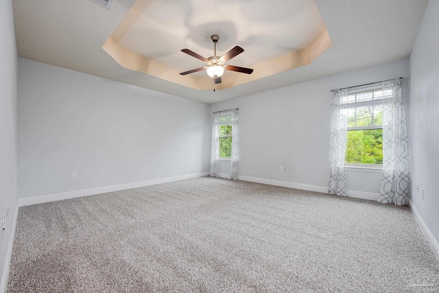 carpeted empty room with a raised ceiling, ceiling fan, and plenty of natural light