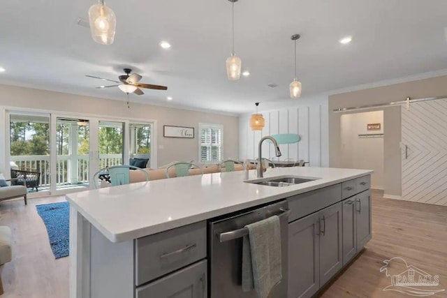 kitchen featuring an island with sink, sink, dishwasher, light wood-type flooring, and a barn door