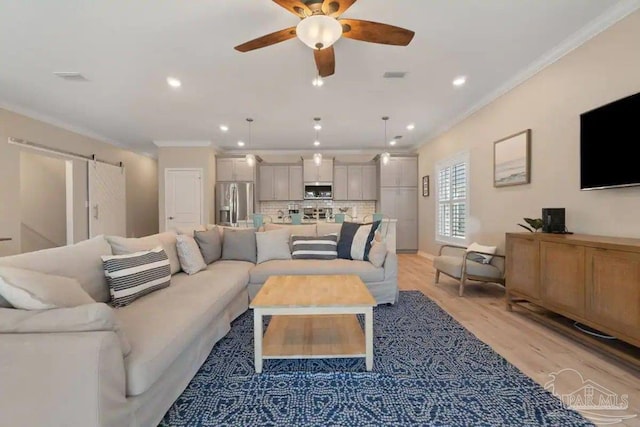 living room with ceiling fan, light wood-type flooring, crown molding, and a barn door