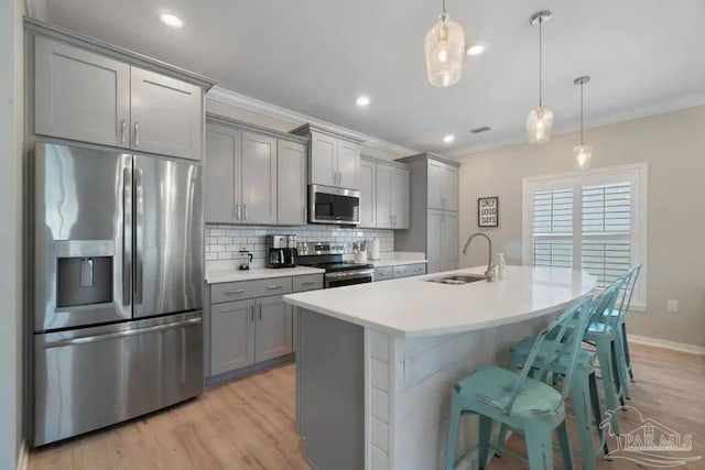 kitchen featuring pendant lighting, gray cabinets, stainless steel appliances, a kitchen bar, and sink