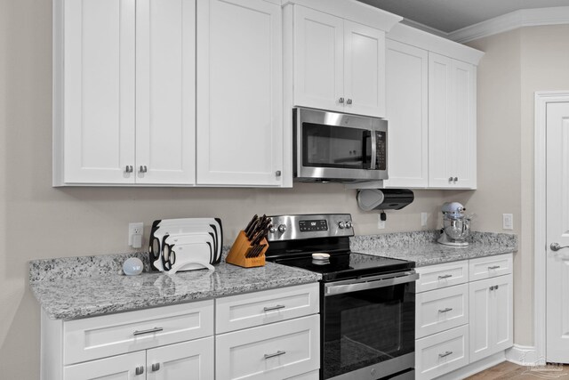 kitchen with appliances with stainless steel finishes, white cabinets, crown molding, and light stone counters