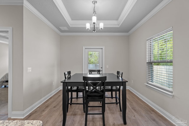 dining room with healthy amount of natural light, a raised ceiling, light wood finished floors, a chandelier, and crown molding