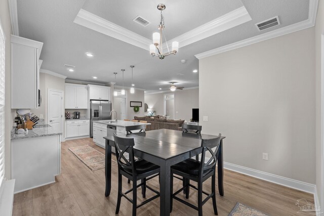 dining area featuring a tray ceiling, ornamental molding, light wood-style floors, a chandelier, and recessed lighting