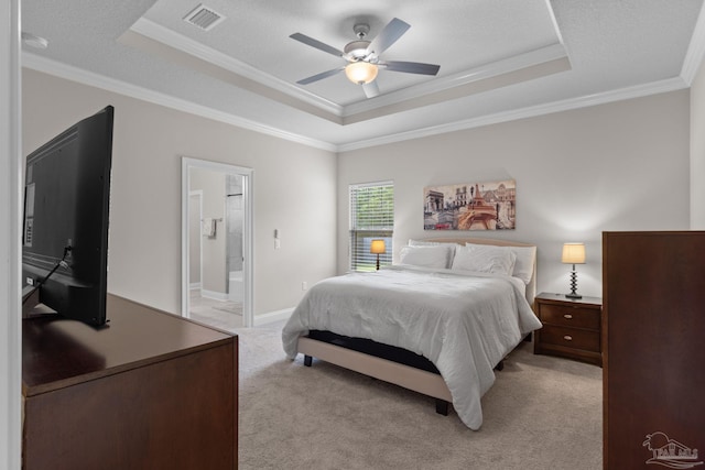 bedroom featuring a tray ceiling, crown molding, light colored carpet, ensuite bath, and ceiling fan