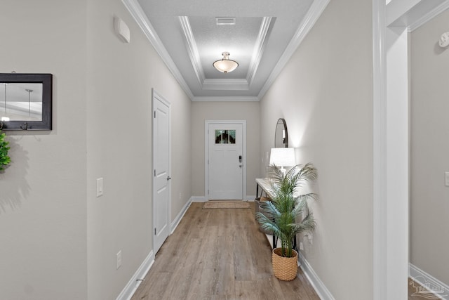entryway with light wood-style floors, a raised ceiling, ornamental molding, and baseboards