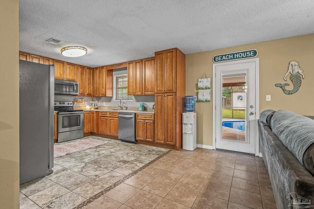 2762 Christine St, Pensacola, FL 32526 - kitchen with stainless steel appliances, brown cabinets, light countertops, a textured ceiling, and light tile patterned flooring