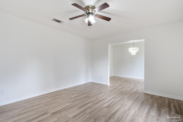 empty room with ceiling fan with notable chandelier and light hardwood / wood-style flooring