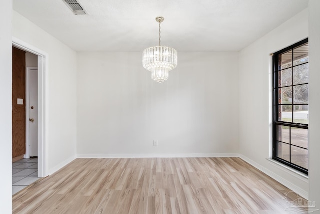 spare room featuring an inviting chandelier and light hardwood / wood-style flooring