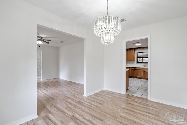 unfurnished dining area with ceiling fan with notable chandelier and light wood-type flooring