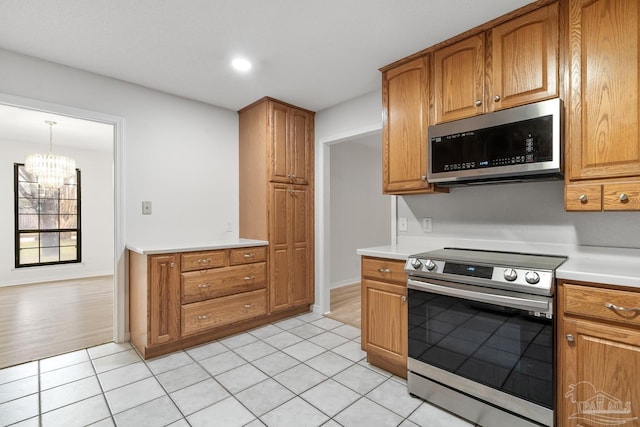 kitchen with appliances with stainless steel finishes, pendant lighting, light tile patterned floors, and a notable chandelier