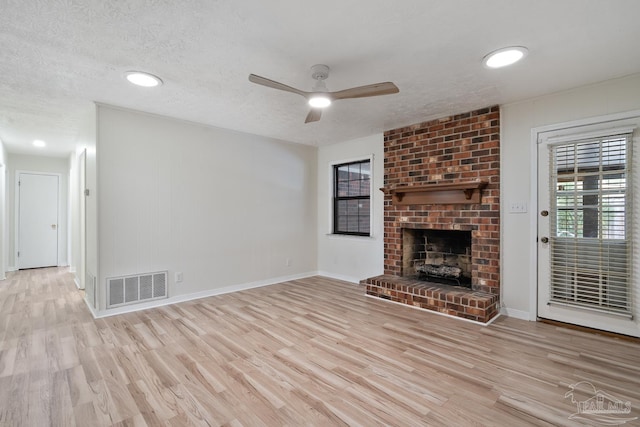 unfurnished living room with ceiling fan, a textured ceiling, a fireplace, and light hardwood / wood-style floors