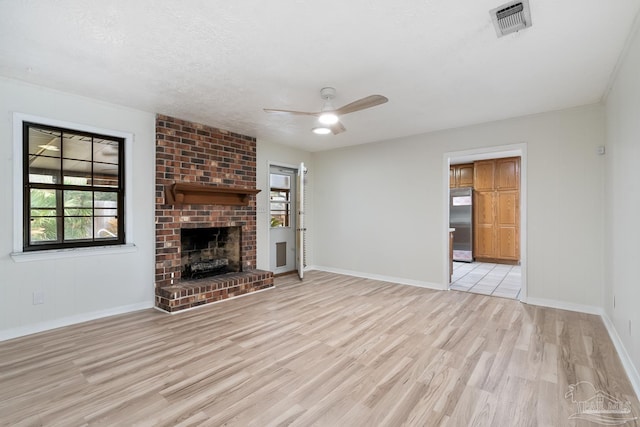 unfurnished living room with ceiling fan, light hardwood / wood-style floors, a brick fireplace, and a textured ceiling