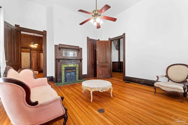 living room with a high end fireplace, light hardwood / wood-style floors, ceiling fan, and a high ceiling