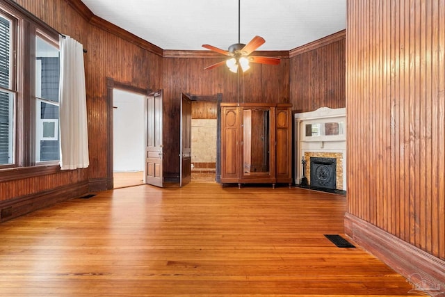 unfurnished living room featuring ceiling fan, wooden walls, and light hardwood / wood-style flooring