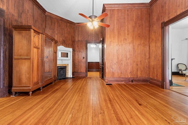 unfurnished living room featuring ceiling fan, light wood-type flooring, and wood walls