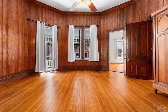 spare room featuring ceiling fan, a healthy amount of sunlight, light hardwood / wood-style flooring, and wood walls