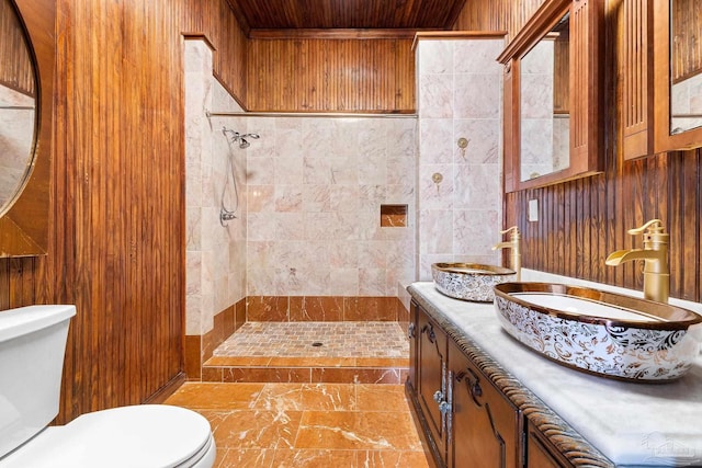 bathroom with vanity, tiled shower, tile walls, and toilet