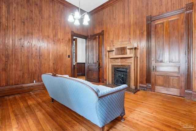 living room featuring a stone fireplace, hardwood / wood-style floors, a chandelier, and wood walls