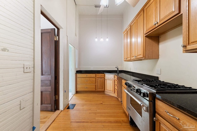 kitchen featuring ceiling fan, high end stainless steel range oven, decorative light fixtures, dark stone counters, and light wood-type flooring