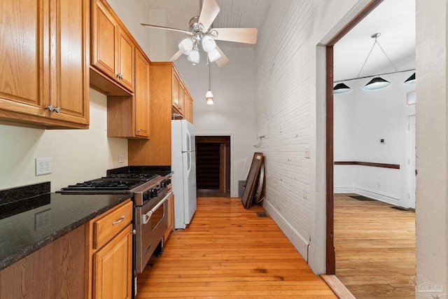 kitchen with brick wall, stainless steel stove, dark stone counters, white fridge, and light wood-type flooring