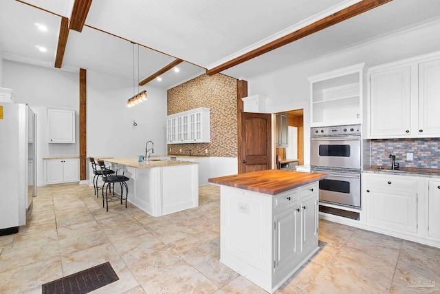 kitchen with double oven, decorative light fixtures, white cabinets, backsplash, and a kitchen island with sink