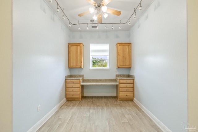 unfurnished office with ceiling fan, rail lighting, built in desk, and light wood-type flooring