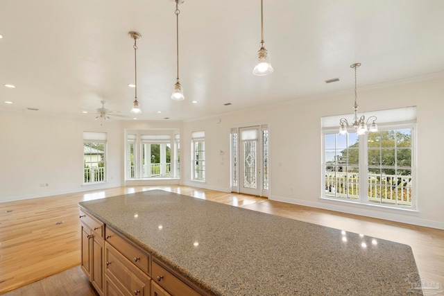 kitchen with pendant lighting, ceiling fan with notable chandelier, light wood-type flooring, and dark stone counters