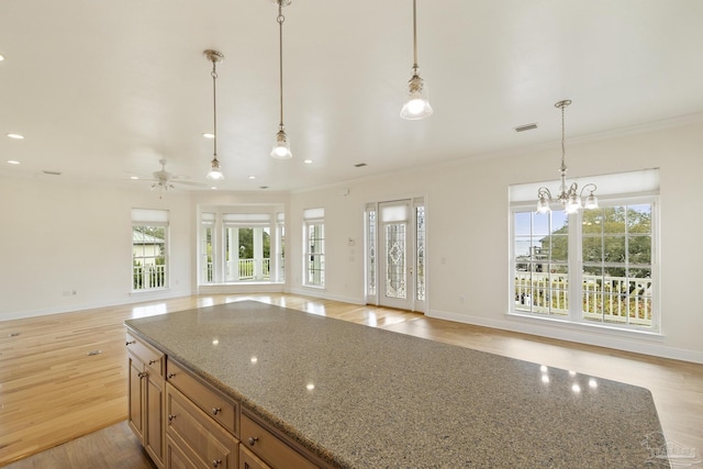 kitchen with stone counters, ornamental molding, pendant lighting, and light wood-type flooring