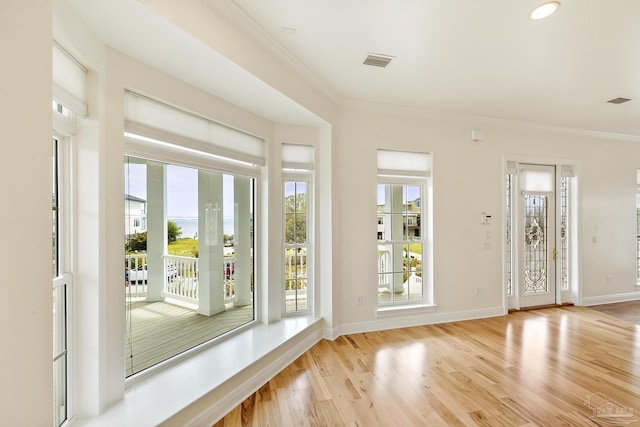 doorway to outside with plenty of natural light, ornamental molding, and light wood-type flooring