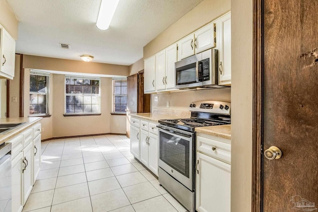 kitchen featuring a textured ceiling, stainless steel appliances, sink, light tile patterned floors, and white cabinets